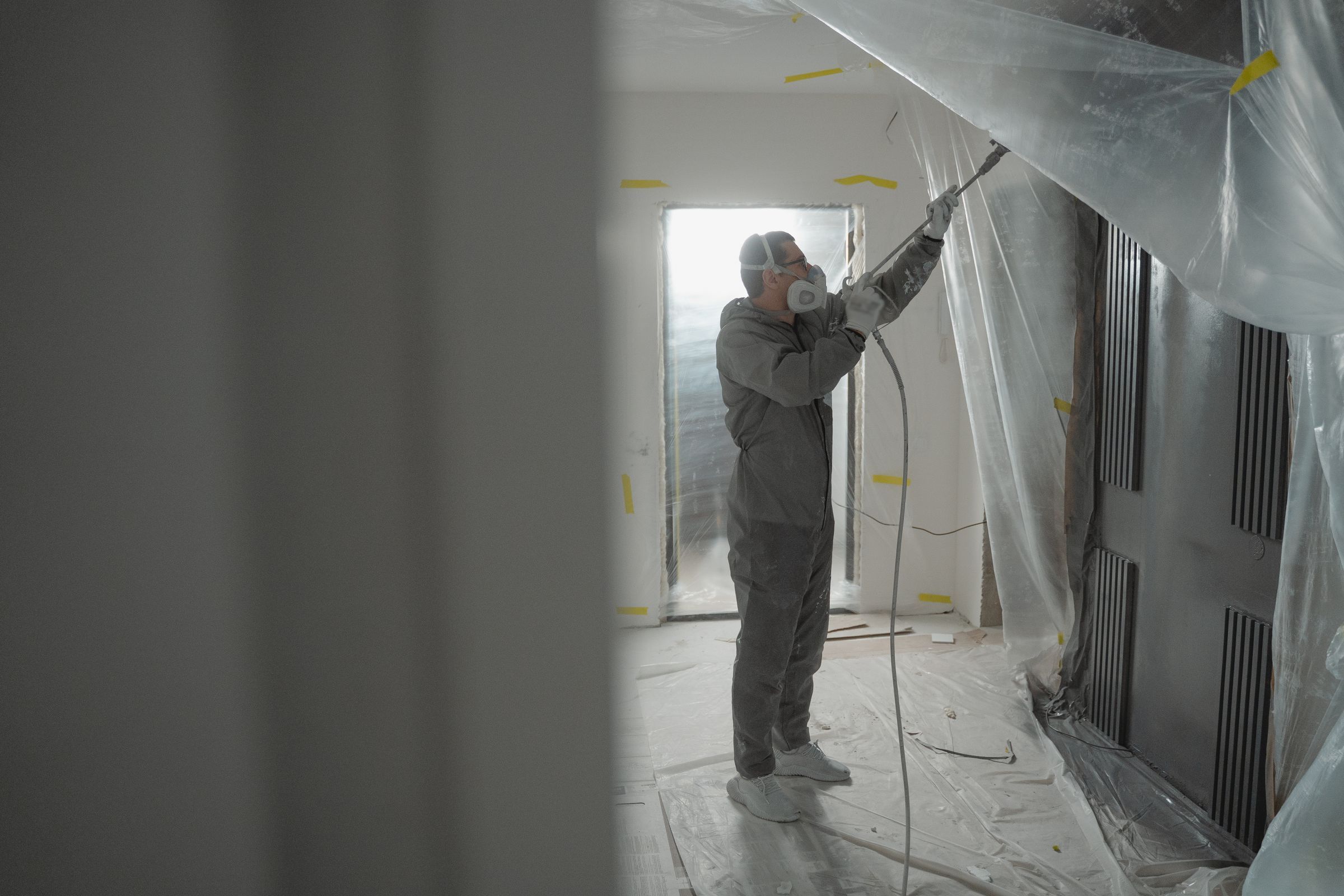 Abatement worker in a white protective suit and respirator inside a sealed work area