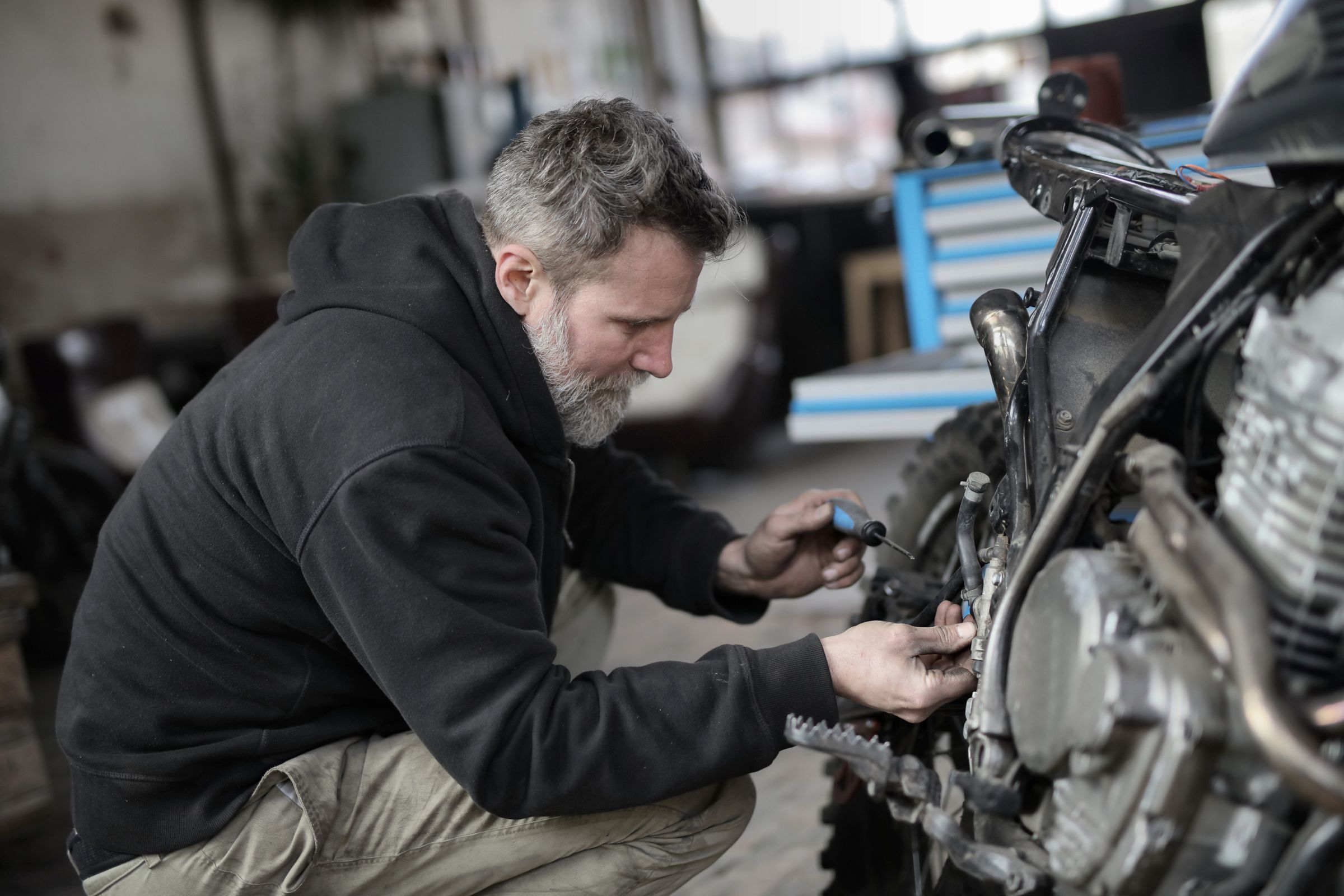 Man kneeling beside a motorcycle, working on it in a garage